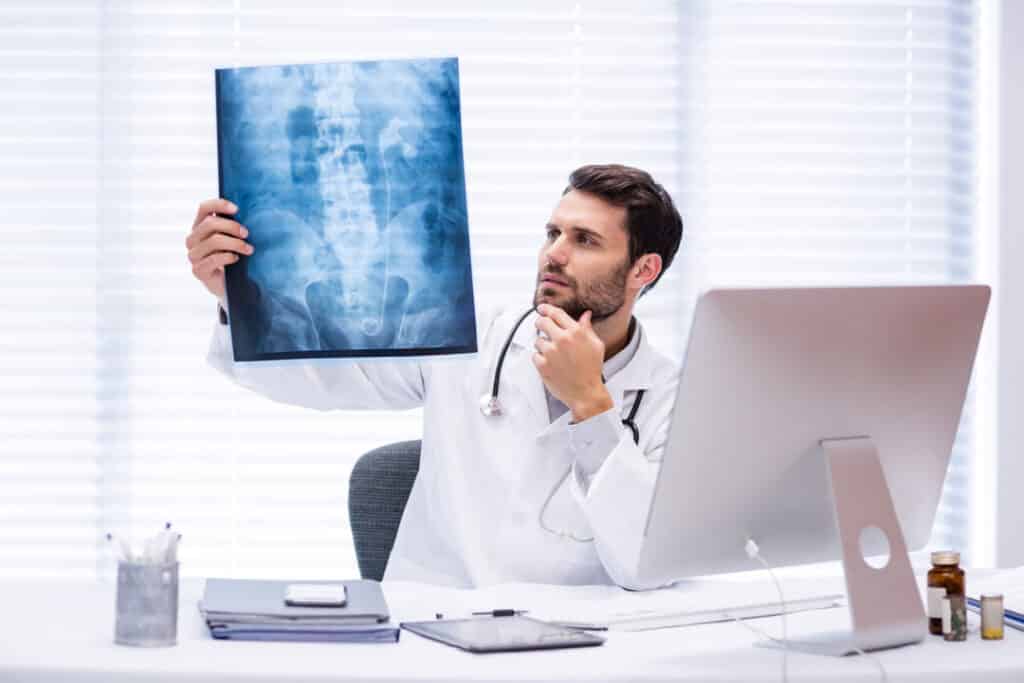 A doctor utilizing digital radiography technology holds up an x-ray image in front of a computer.