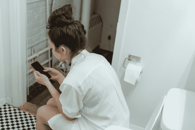 A woman looking at her phone in a bathroom, distracted by information on "how to clean private parts after urination.