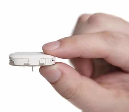 A person's hand holding a tubeless insulin pump on a white background.